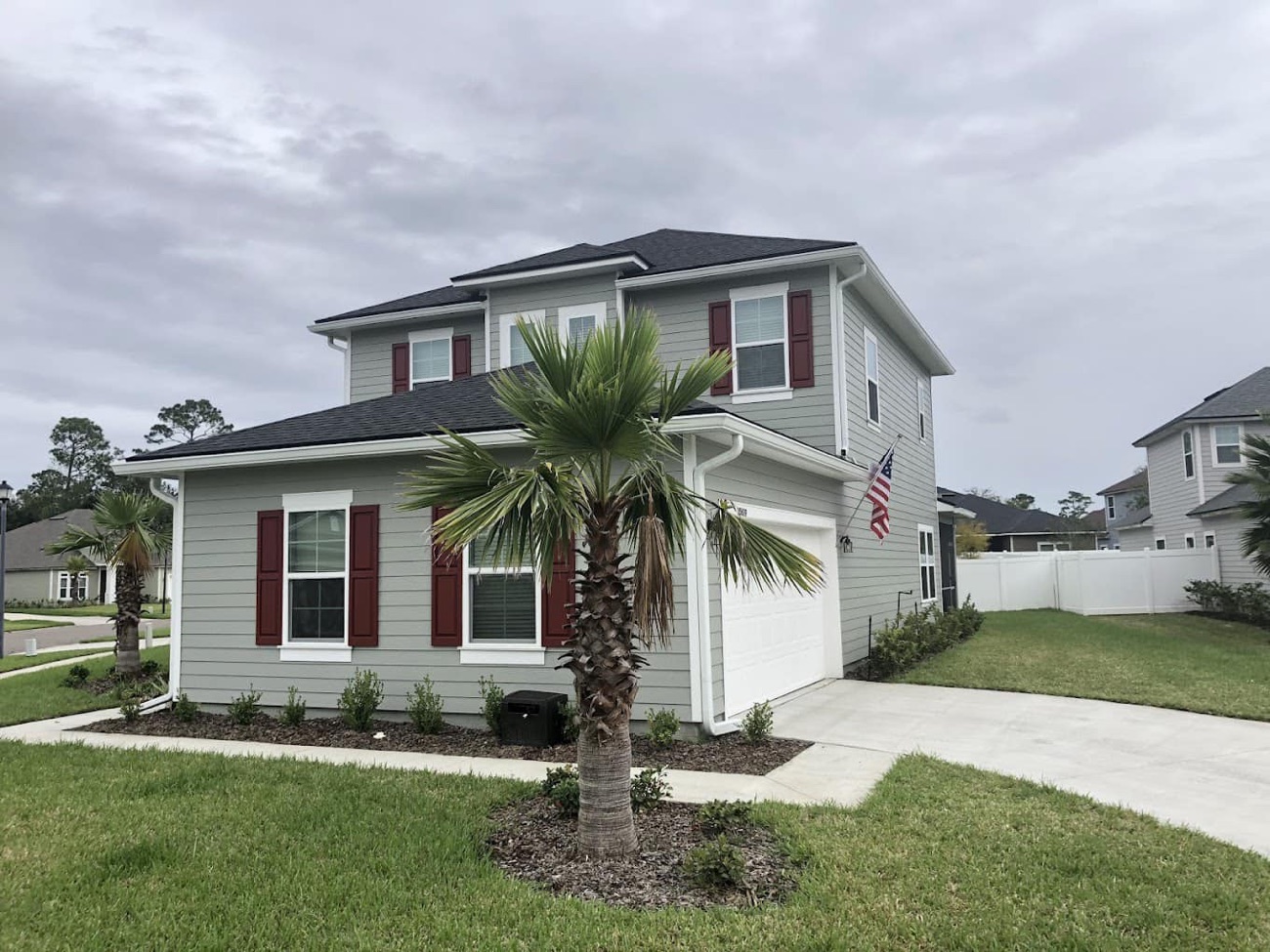 White seamless rain gutters and downspouts installed along the roofline of a two-story Northeast Florida home flying an American flag — Aqua Premier seamless gutter installation in Ponte Vedra Beach, Nocatee, St. Augustine, Jacksonville & Clay County, FL